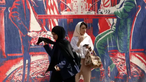 EPA Two women walk next to an anti-US mural near the former US embassy in Tehran