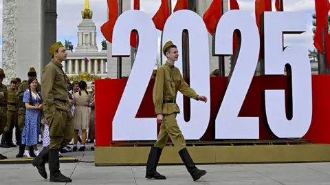 Getty Images Students dressed in old Soviet costumes stand in front of a large sign saying 2025 as they mark the 80th anniversary of the end World War Two