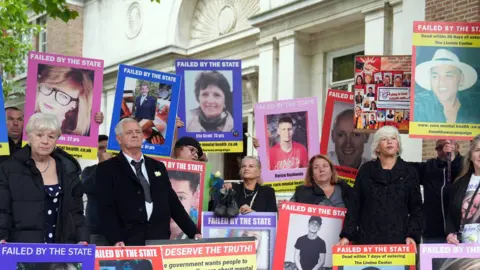 PA The families of those who have died while in the care of mental health services in Essex stand outside the inquiry protesting. There are around 20 people in the image which shows them standing with placards held against them and large posters of their loved ones. They show a range of faces, both men and women and young and old. One reads "failed by the state".