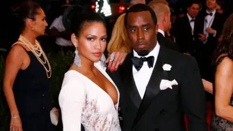 Reuters Cassie, in large diamond dangly earrings and a white gown, puts her arm on the shoulder of Sean Combs, who wears a black tuxedo with a black bowtie and white pocket square. 