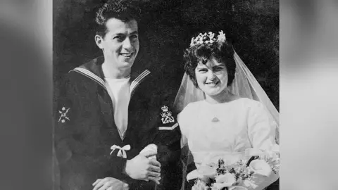 Family photo A wedding photo from 1959 of Ernest and Wendy Williams. She is wearing a white wedding dress and he is wearing a Navy uniform.