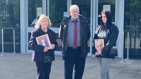 Three members of Jodey Whiting's family - with mother Joy Dove on the left - outside Teesside Coroner's Court as a second inquest into her death opens. Two of them are holding framed photos of Jodey.    