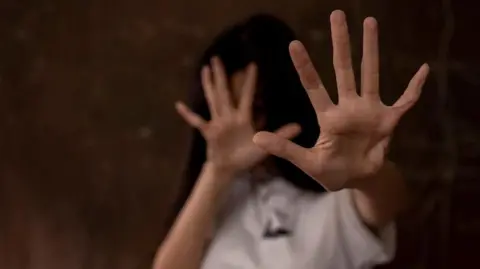 Getty Images Woman holding her arms in front of her head in self defence.