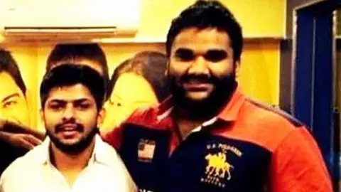 Goldy and Lawrence both smile for the camera - Goldy Brar is tall, bearded with heavy eyebrows and is wearing a colourful Polo shirt 