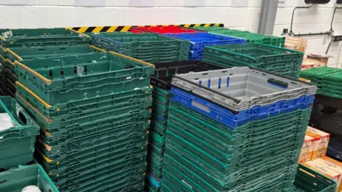 BBC News The photo shows towers of different coloured empty crates stacked on top of each other. Each stack contains 15 to 20 crates. 