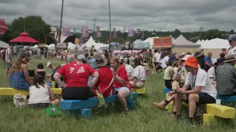 A crowd of people sit on painted benches whilst talking to one another at the festival 