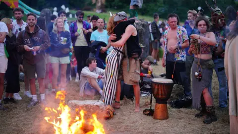 Ben Birchall/PA Two people hugging next to a fire, surrounded by other people.