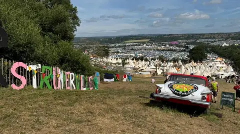 Strummerville sign on a fence at the top of a hill. It overlooks the tipi area of Glastonbury Festival. 