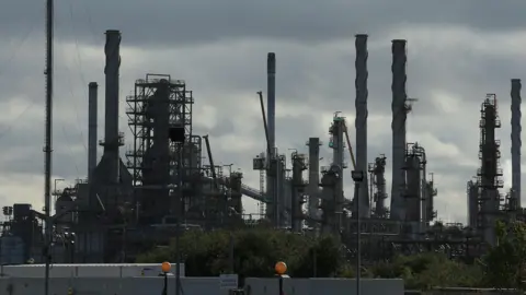 Getty Images The Prax Lindsey Oil Refinery. A cluster of metal structures rising to the grey sky.
