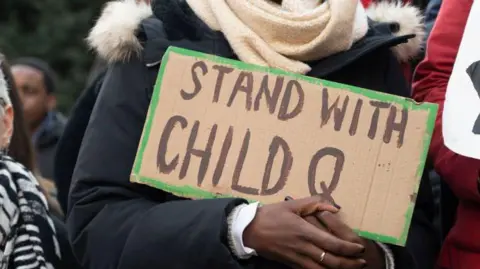 Getty Images A close up of a person holding a cardboard placard stating "stand with Child Q" at a protest.