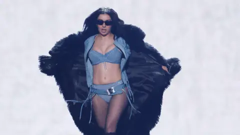Getty Images Charlie XCX performing at the Grammy Awards in February wearing a light denim bikini and a large fake fur black coat with black sunglasses