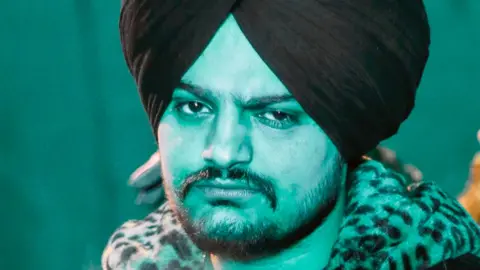 BBC Sidhu Moose Wala stares into the camera in a promotional shot - he wears a black turban and has a leopard skin collar 