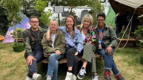 BBC (Left to Right) - Jonathan Rothery, Alison Howe, Emily Eavis, Zoe Ball, Lorna Clarke all sat on a bench backstage at Glastonbury Festival.
