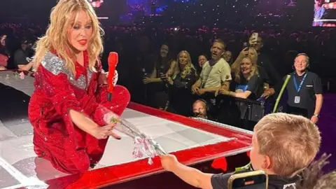 Glen Frost Kylie Minogue on stage in Birmingham being handed a pink rose by three-year-old fan Reuben