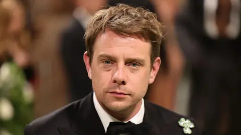 Getty Images A close-up image of Jonathan Anderson pictured at the Met Gala in 2024. He has short brown hair and has a neutral expression on his face. He is wearing a black suit jacket with a shamrock broach on his shoulder.
