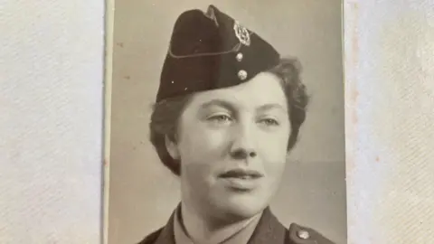 Supplied Doreen Lemon, in World War II uniform, with a hat and hair tied back. The image is in black and white.  