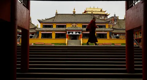 Xiqing Wang/ BBC A red-robed monk walks past the gates to a monastery in Aba