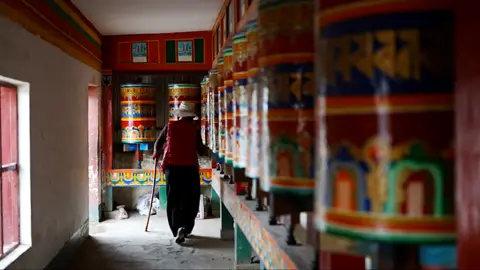 Xiqing Wang/ BBC A woman walks past colourful prayer wheels depicting murals from the Buddha's life inside the Kirti monastery