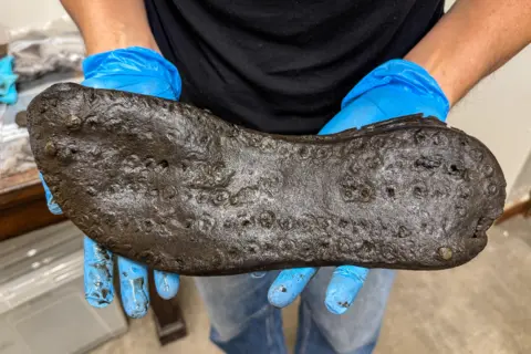 The Vindolanda Trust The sole of a large black shoe in the blue gloved hands of a person.
