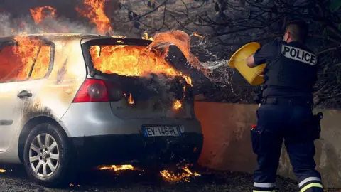 Getty Images A police officer tries to put out a fire in a car during a wildfire
