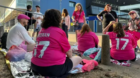 Cameron Noble/BBC A group of Ed Sheeran fans - some standing, some sitting on the ground - outside Portman Road. Most of them are wearing pink tops 