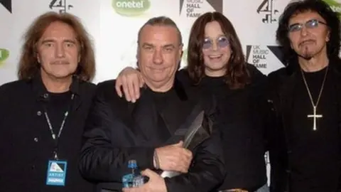 PA Black Sabbath band members smiling at the camera, all wearing black clothes.