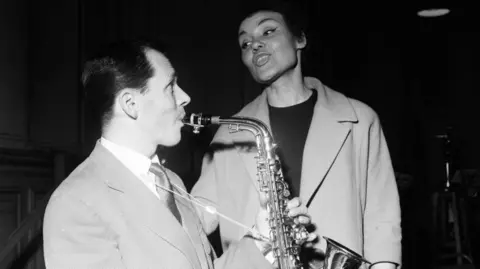 Getty Images Cleo Laine and John Dankworth photographed in the 1950s; he is playing a saxophone and she is singing