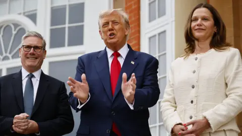 EPA Keir Starmer meets the US president with his wife Victoria. Trump is wearing a blue suit with a red tie, Starmer is wearing a dark jacket and blue tie and Mrs Starmer is wearing a cream suit. 