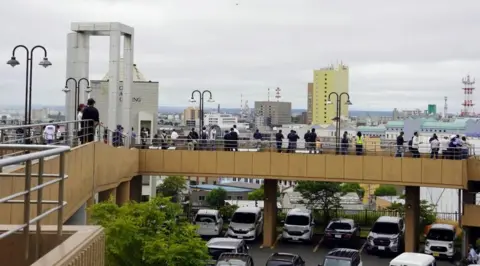 Reuters People standing on a raised pedestrian overpass, which is on top of a carpark. They are looking out over the city.