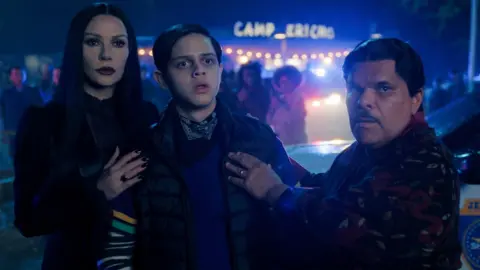 Netflix Catherine Zeta-Jones as Morticia Addams, Isaac Ordonez as Pugsley Addams, Luis Guzmán as Gomez Addams in season two of Wednesday.