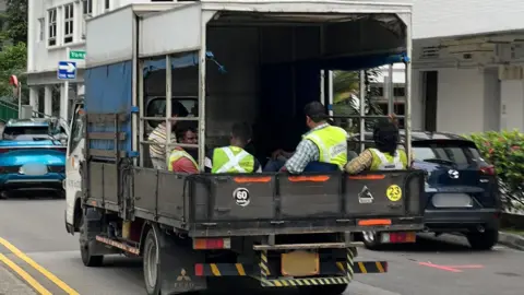 BBC/Gavin Butler A group of migrant workers sitting at the back of a lorry in Singapore