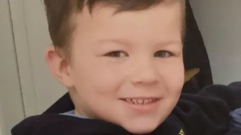 Family photo Caio, the victim of a dog attack, smiling at the camera. The young boy has short brown hair and brown eyes and wearing a dark jumper. 