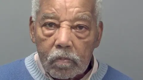 Avon and Somerset Police A man with with grey hair. He is older and has wrinkles. He is wearing a blue knitted top and looking into camera