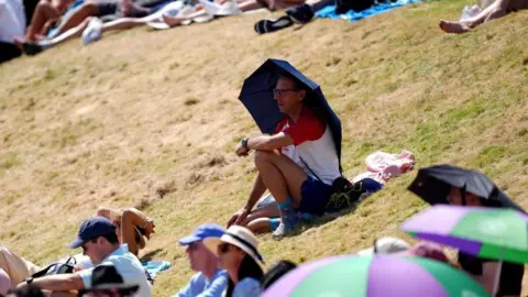 PA A man sitting under a black umbrella on a parched patch of grass