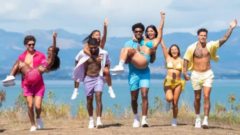Kim Nunneley/Peacock via Getty Images L-R Love Island finalists Nicolas "Nic" Vansteenberghe, Olandria Carthen, Bryan Arenales, Amaya Espinal, Chris Seeley, Huda Mustafa, Iris Kendall, Jose "Pepe" Garcia-Gonzalez. The couples are pictured wearing matching coloured outfits while walking along the coast on a sunny day, the sea and mountains behind them. Nic, Bryan and Chris all carry their partners while Iris and Jose walk hand in hand.