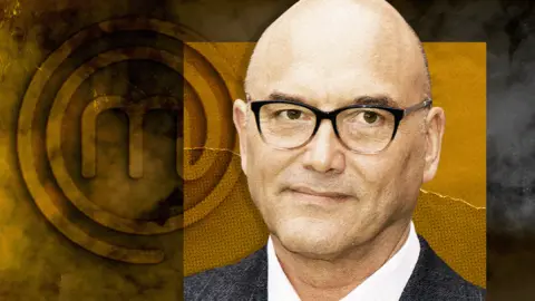 BBC/Getty Images A head and shoulders shot of Gregg Wallace, with a background featuring the MasterChef logo. The background is a mix of dark and golden hues, with the logo prominently displayed on the left side. Gregg Wallace is wearing a suit jacket over a white shirt.