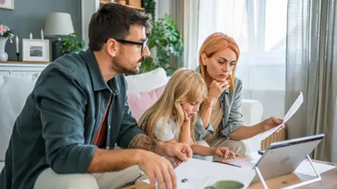 Getty Images A couple sit with a girl on a sofa looking at a laptop and a piece of paper 