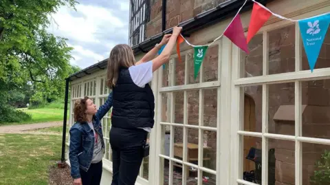 BBC Two women putting up National Trust bunting on the outside of a house
