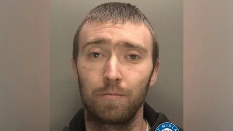 West Midlands Police A mugshot of a man with short, brown hair and a beard. He is staring into the camera and wearing a black hoodie.
 