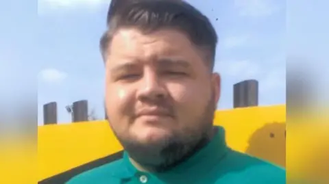 Police Scotland Euan Johnston, a young man with slicked back dark hair and a turquoise green polo shirt, looks into the camera. His eyes are squinting as the sun shines brightly and has a very slight smile. He is standing against a bright yellow wall.