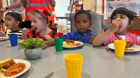 Hayley Clarke / BBC Four nursery pupils sat at a canteen table enjoying their Friday fish and chips dinner at St Mary's Primary in Stoke-on-Trent, including spaghetti hoops. They are in fancy dress for 'aspirations day'.