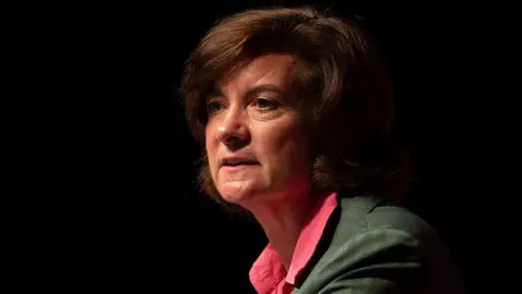 Getty Images A side-shot of Eluned Morgan in front of a dark background, wearing a green suit and a red shirt. She is looking out into space in front of her.