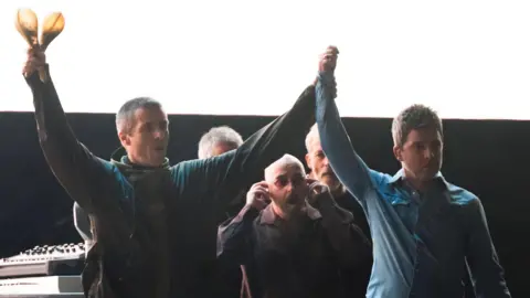 Getty Images Liam and Noel Gallagher raise their hands together as they took to the stage in Cardiff's Principality Stadium