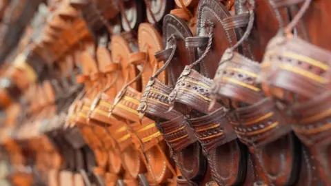 BBC The image shows Kolhapuri sandals in different shades of brown displayed at a shop. 
