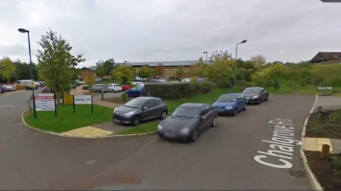 Google A parking area surrounded by trees and bushes. A building is visible in the background. Nearby sign reads "OAKHILL STC"