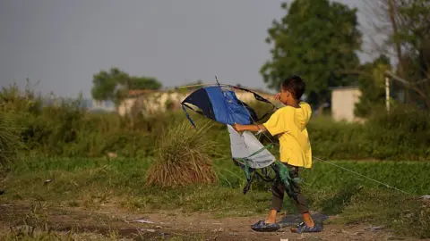 Haryo Bangun Wirawan/BBC Back view of a boy in a yellow T-shirt holding a large blue kite