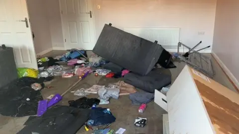 Supplied A ransacked room inside Courtney Mitchell's flat - a sofa can be seen overturned and there are piles of mess and clothing strewn across the floor.