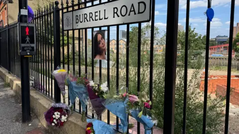George King/BBC Bouquets of flowers attached to black fencing in Burrell Road, Ipswich. A photo of Courtney Mitchell is also attached. 