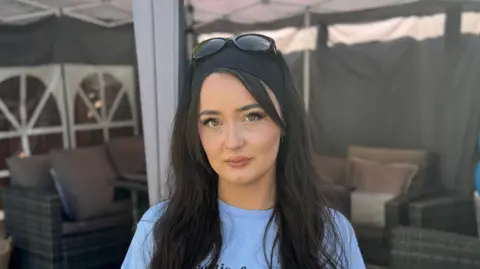 George King/BBC A head and shoulders image of Charleigh Mitchell. She has long black hair and is looking into the camera. She is standing in a garden and wearing a light blue T-shirt. 
