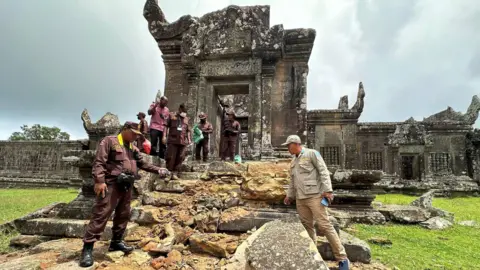 Cambodian Mine Action Centre (CMAC) Cambodian officials point to what appears to be broken steps leading up to an old Khmer temple - rubble from broken stones can be seen in the picture. 